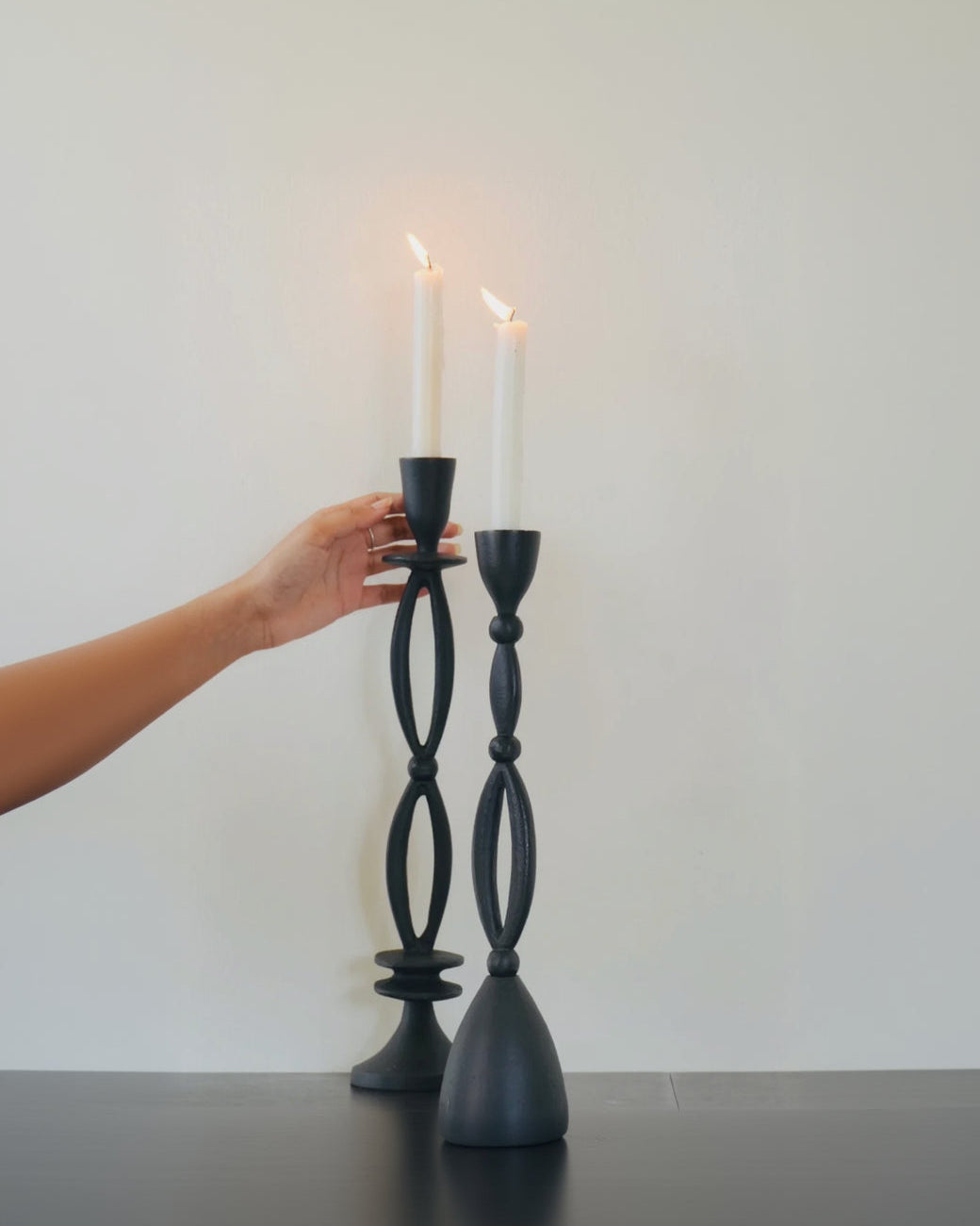 Black candle holders with lit candles against a plain background