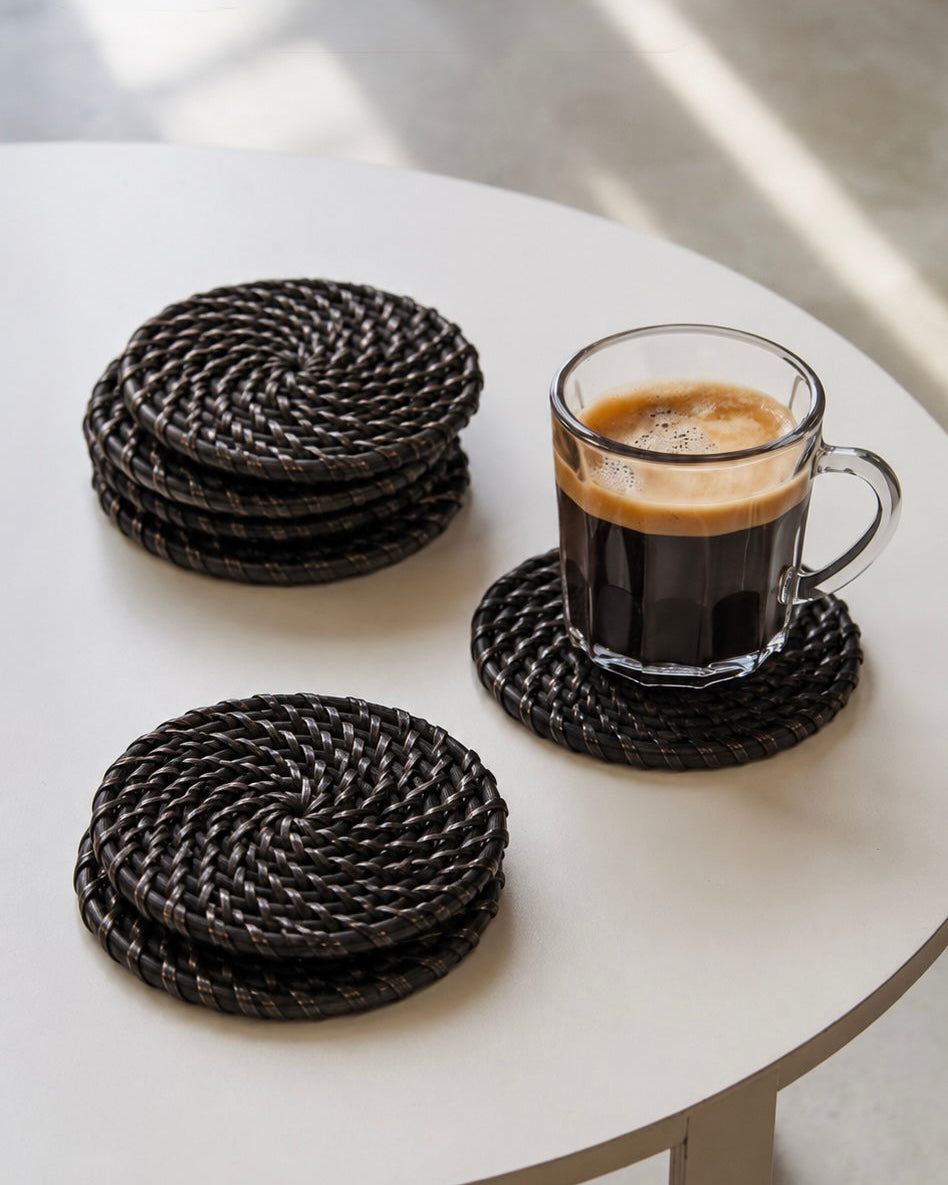 Three round woven black and white coasters on a white round table, with one coaster holding a glass mug of espresso and two coasters stacked.