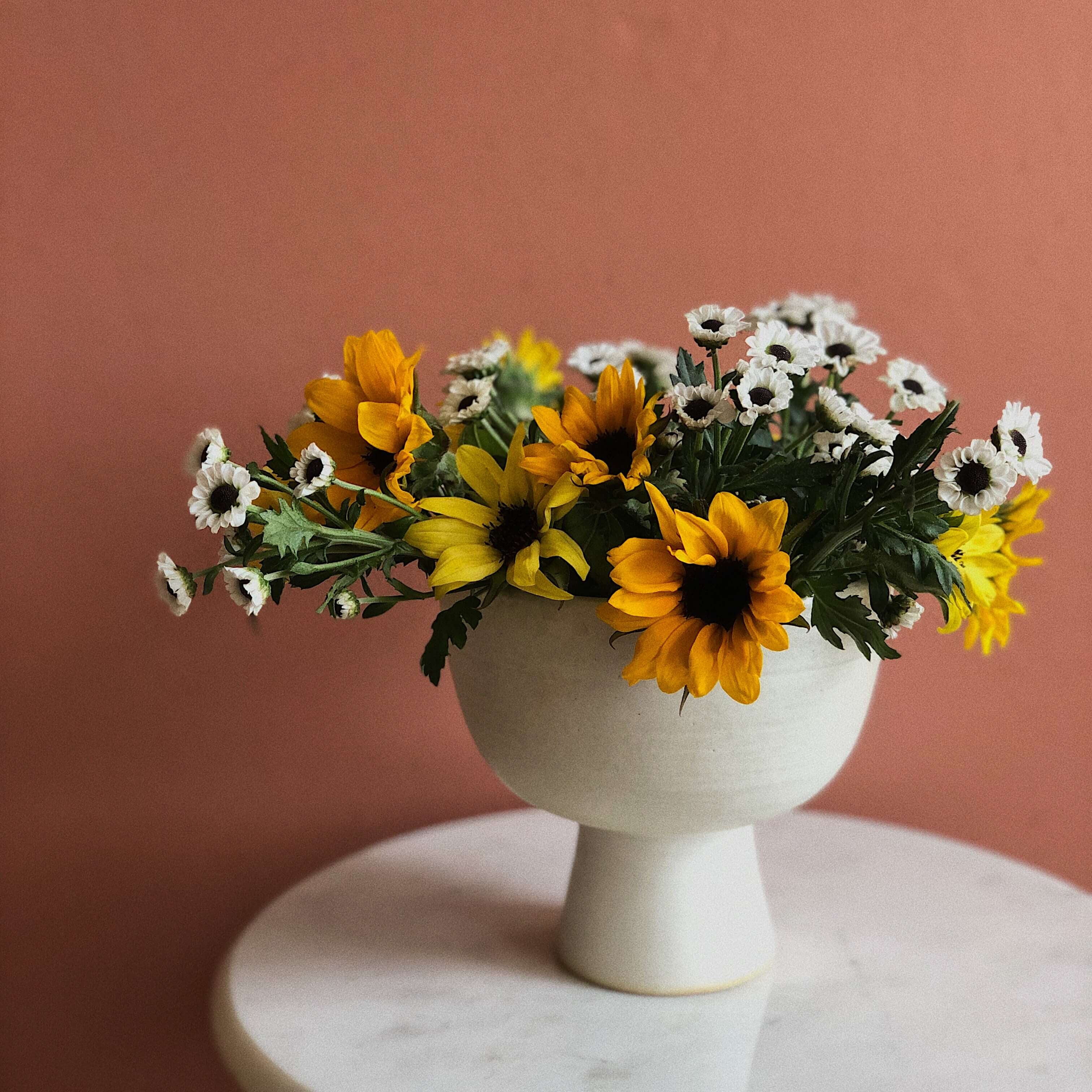 White vase with sunflowers and daisies on a pink background