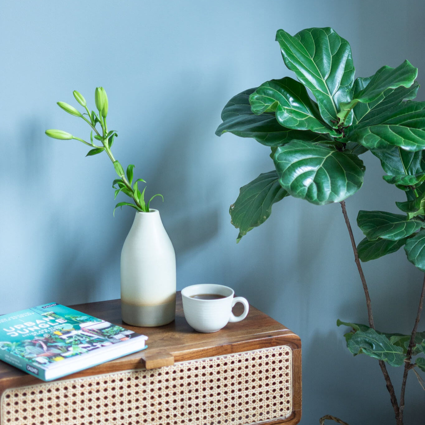 Wooden side table with a vase, cup, and book against a light blue wall